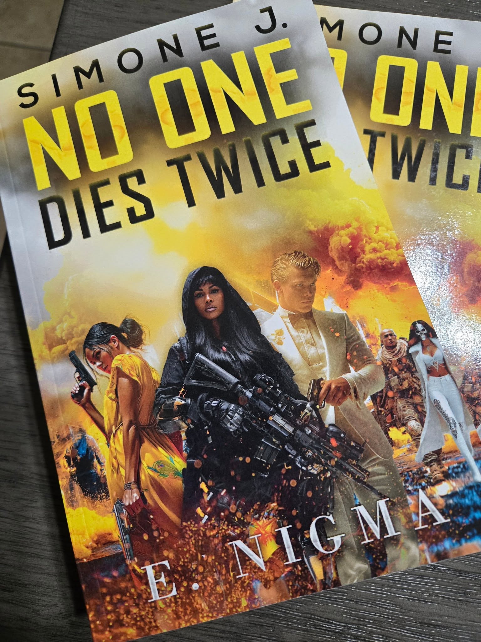 Book cover titled 'No One Dies Twice' by Simone J. features a woman with a gun, surrounded by people and explosions.