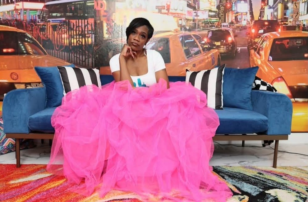 Young girl sitting on a blue sofa with pink tulle skirt, city street background, colorful rugs, and striped pillows.