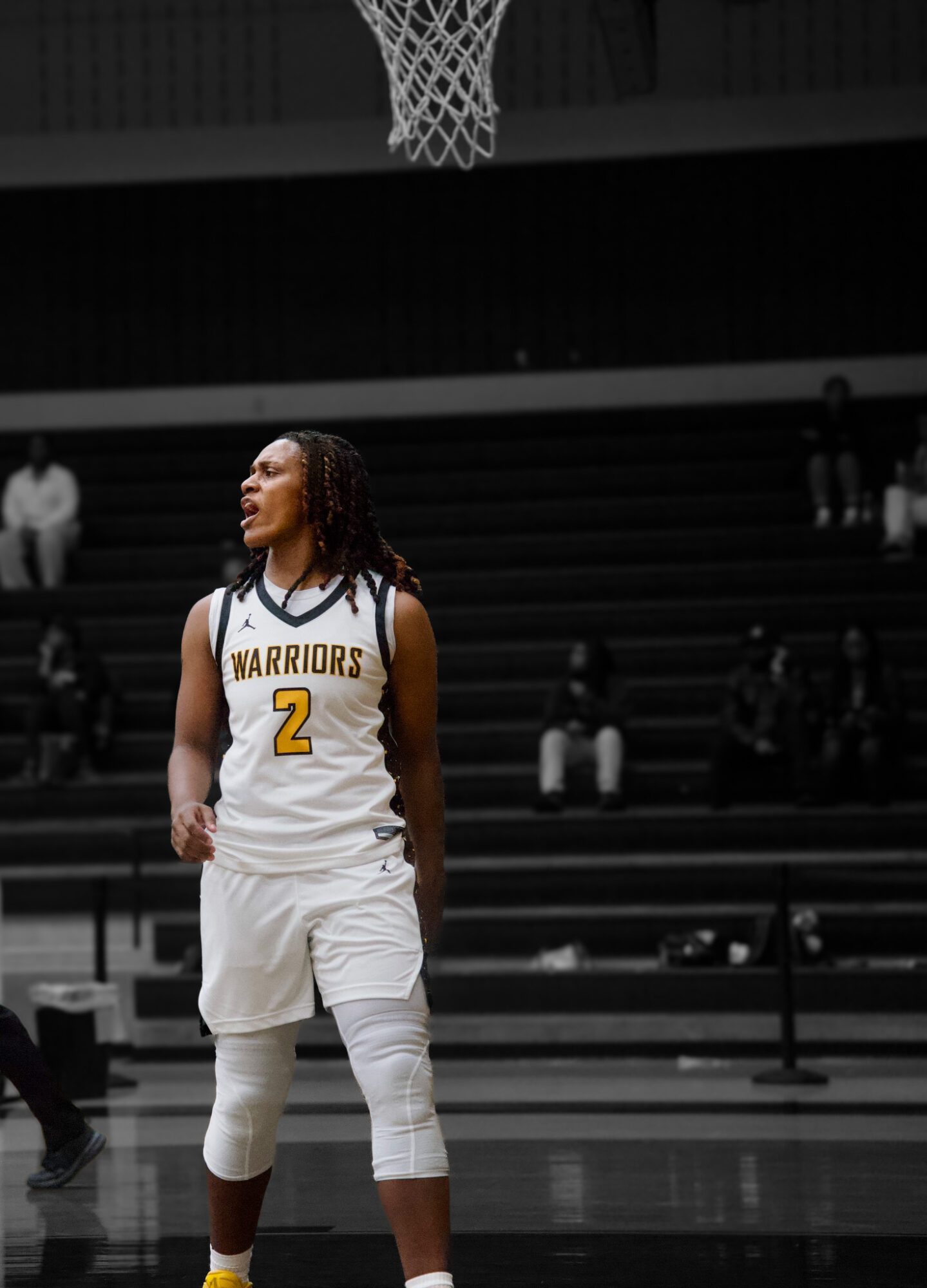 Basketball player wearing a Warriors jersey with number 2 stands on the court, looking to the side, with spectators in the background.