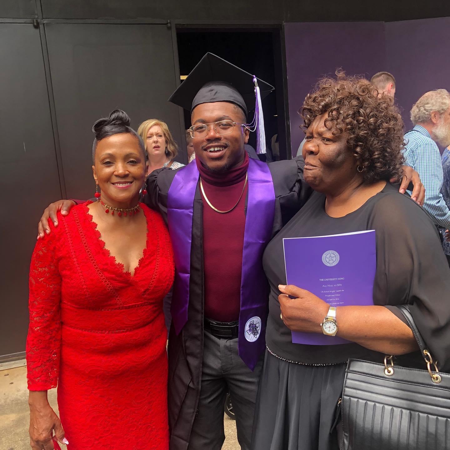 Three people celebrating graduation, with one in a cap and gown, smiling and holding a diploma, in a group photo.