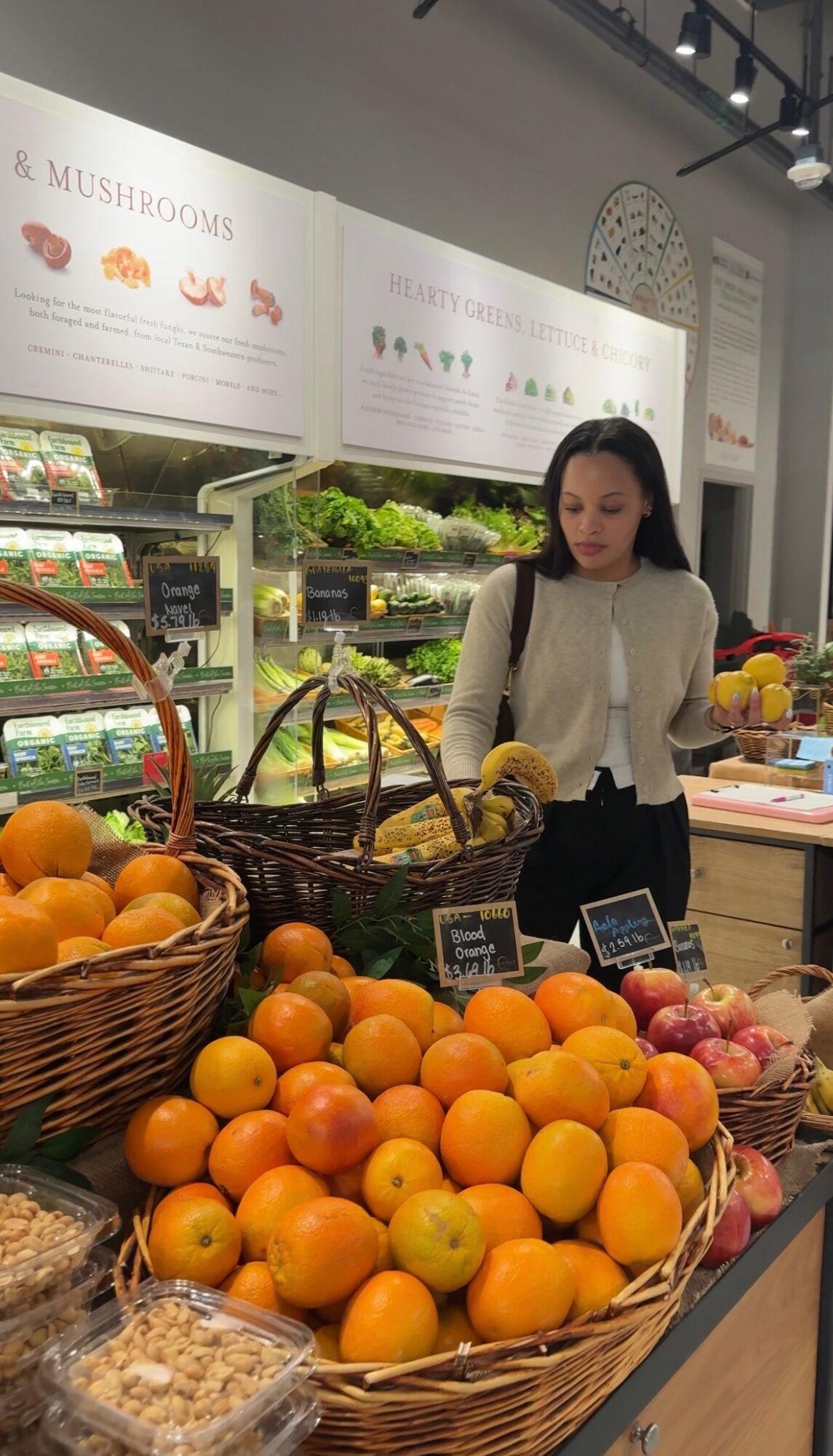 Woman shopping for oranges and other produce at a grocery store, with baskets of fruit and vegetables around her.