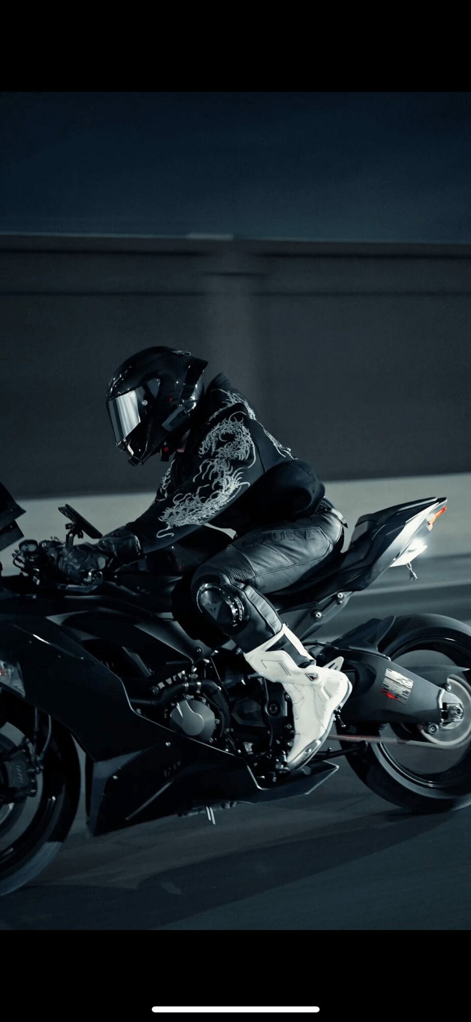 Motorcycle rider wearing helmet and gear, riding on a dark road at night.