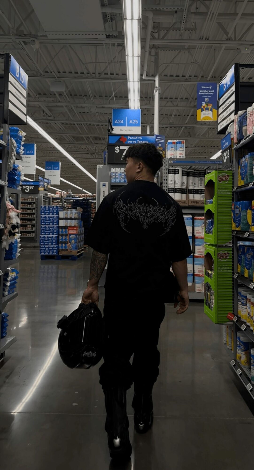 Person walking in a store aisle carrying a bag, shelves with products on both sides, ceiling lights overhead.