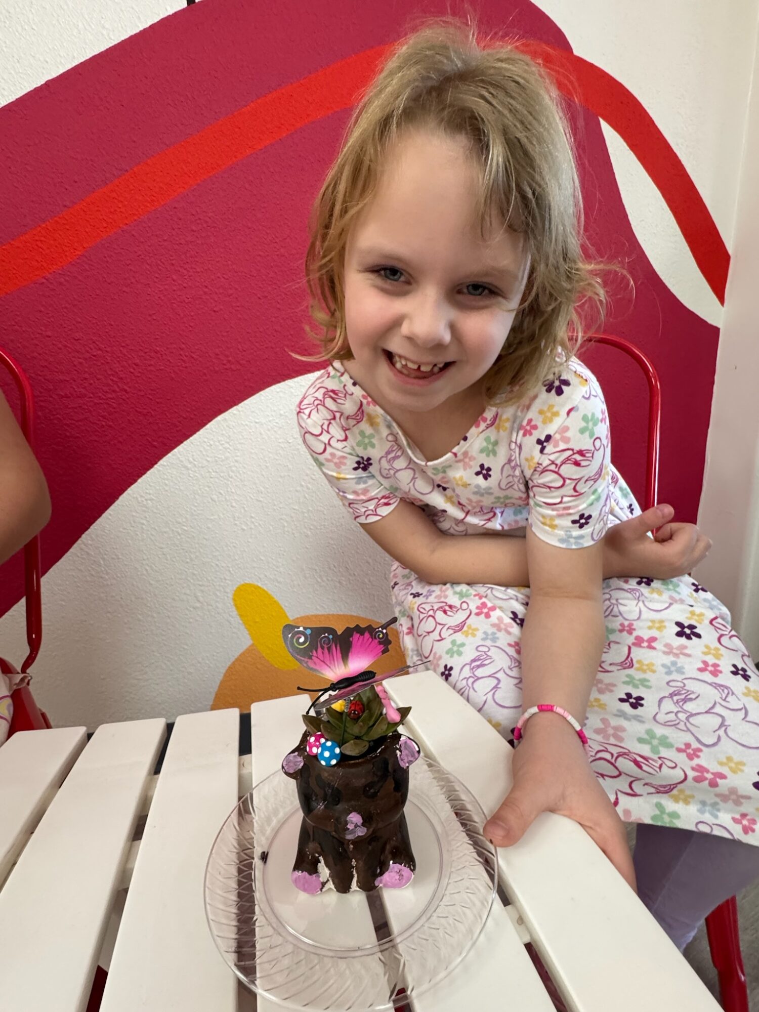 Young girl with curly hair smiling, sitting at a table with a small dog figurine on a plate, colorful background.