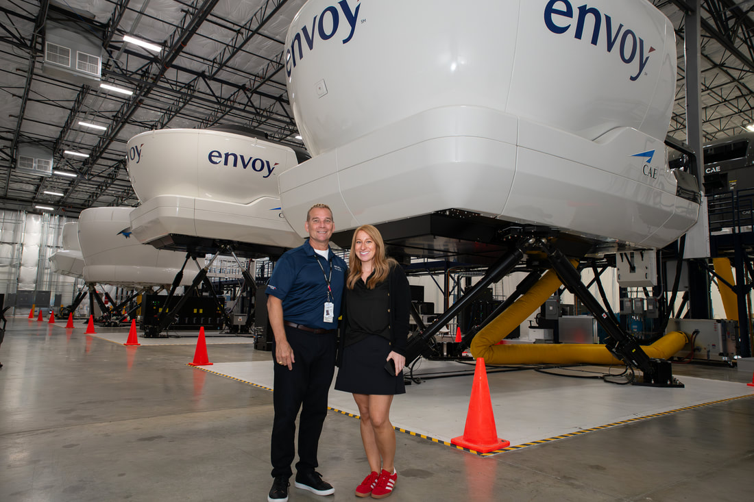 Two people standing inside a large industrial space with spacecraft components labeled 'envoy' behind them.