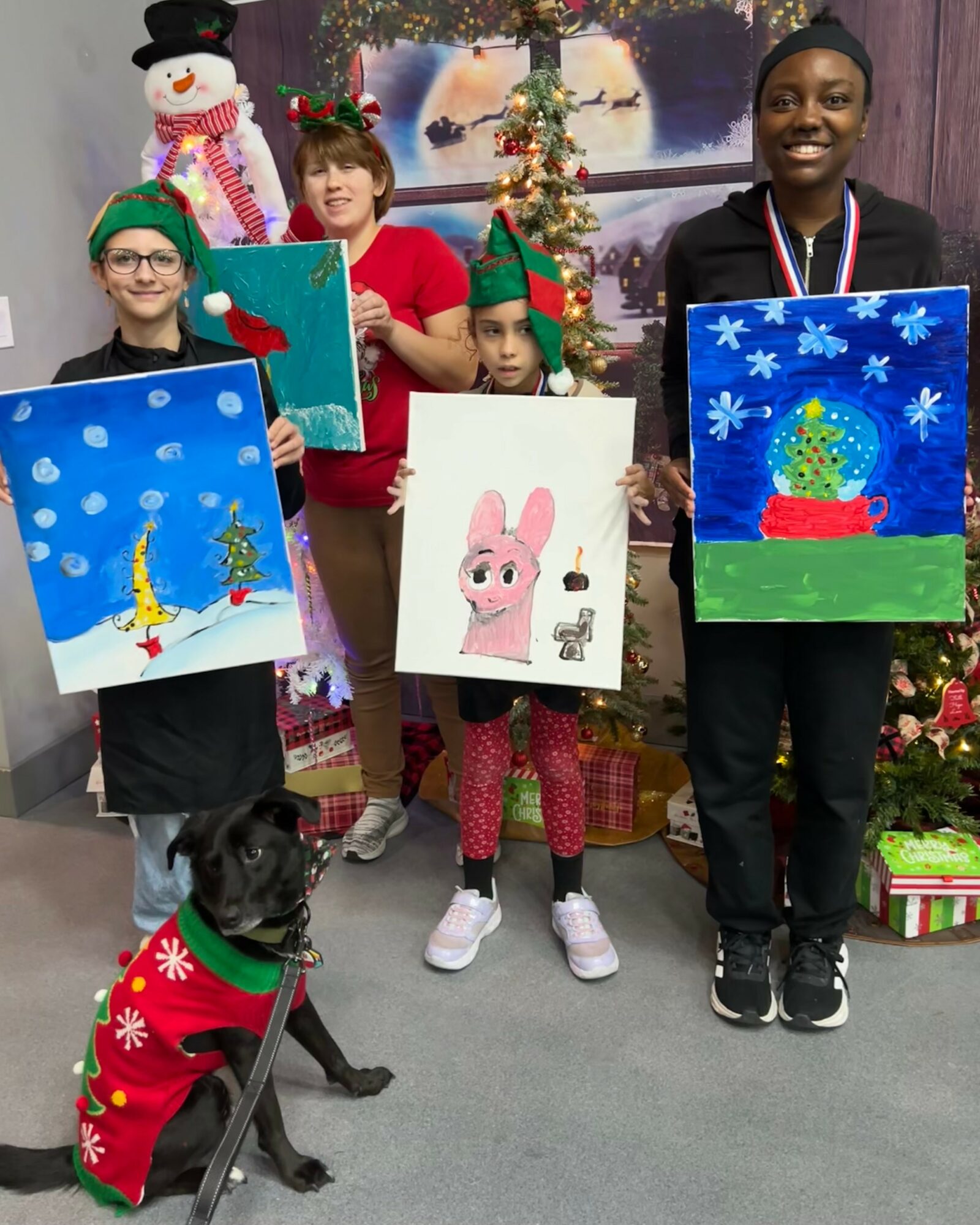 Four children and a dog pose with Christmas paintings, a decorated tree, and festive decorations in the background.