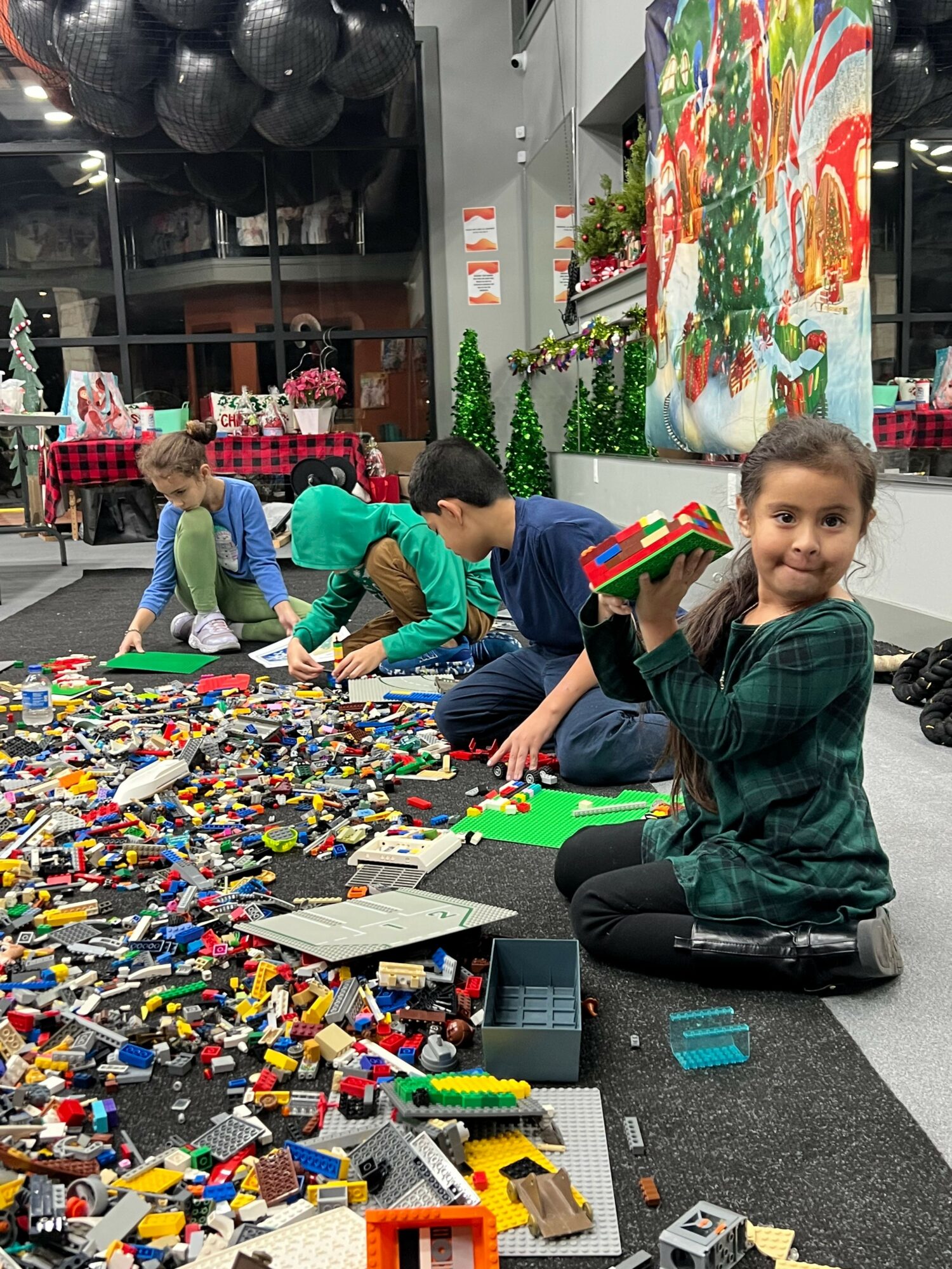 Children playing with colorful building blocks and toys on a table in a room decorated with a Christmas tree.