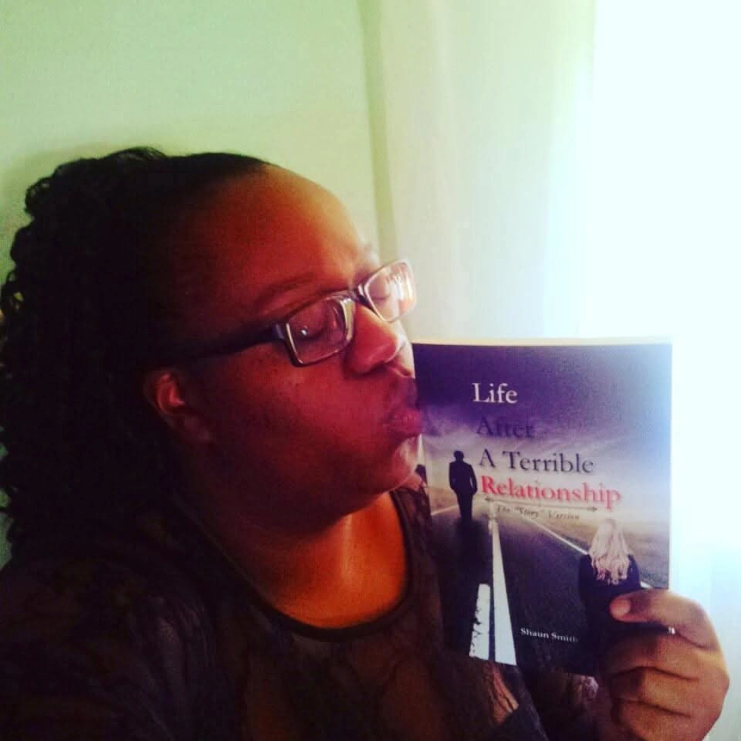 Woman with glasses reading a book titled 'Life: A Terrible Relationship' indoors, light coming from the right side.
