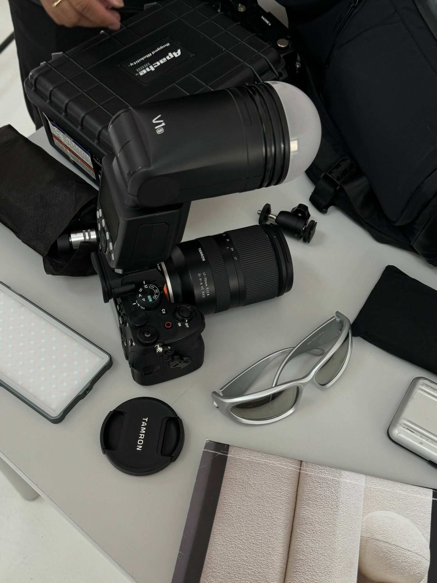 Camera with large lens, sunglasses, and various electronic accessories on a white surface.