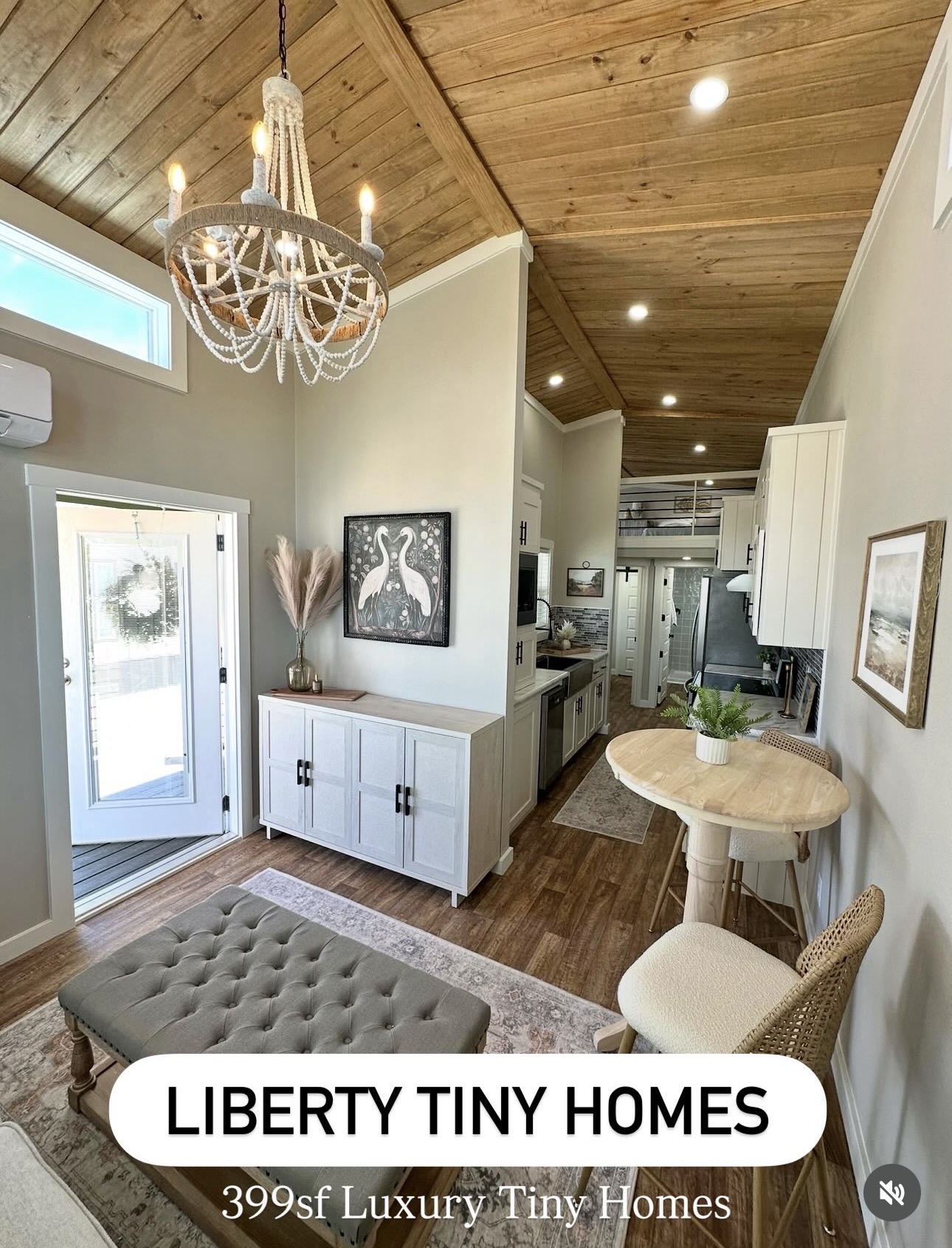 Living area with a tufted ottoman, white cabinet, artwork, and a round table with a chair, wooden ceiling, and door to outside.
