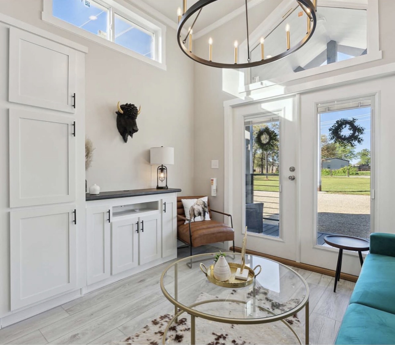 Bright entryway with white cabinets, a brown chair, glass door, and large windows showing outdoor scenery.