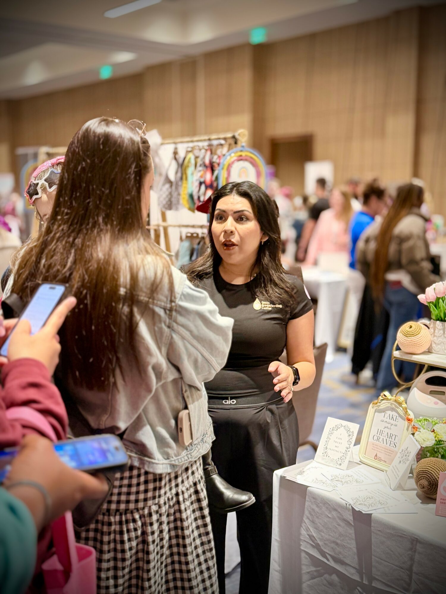 Two women are talking at an indoor event with booths and displays in the background.