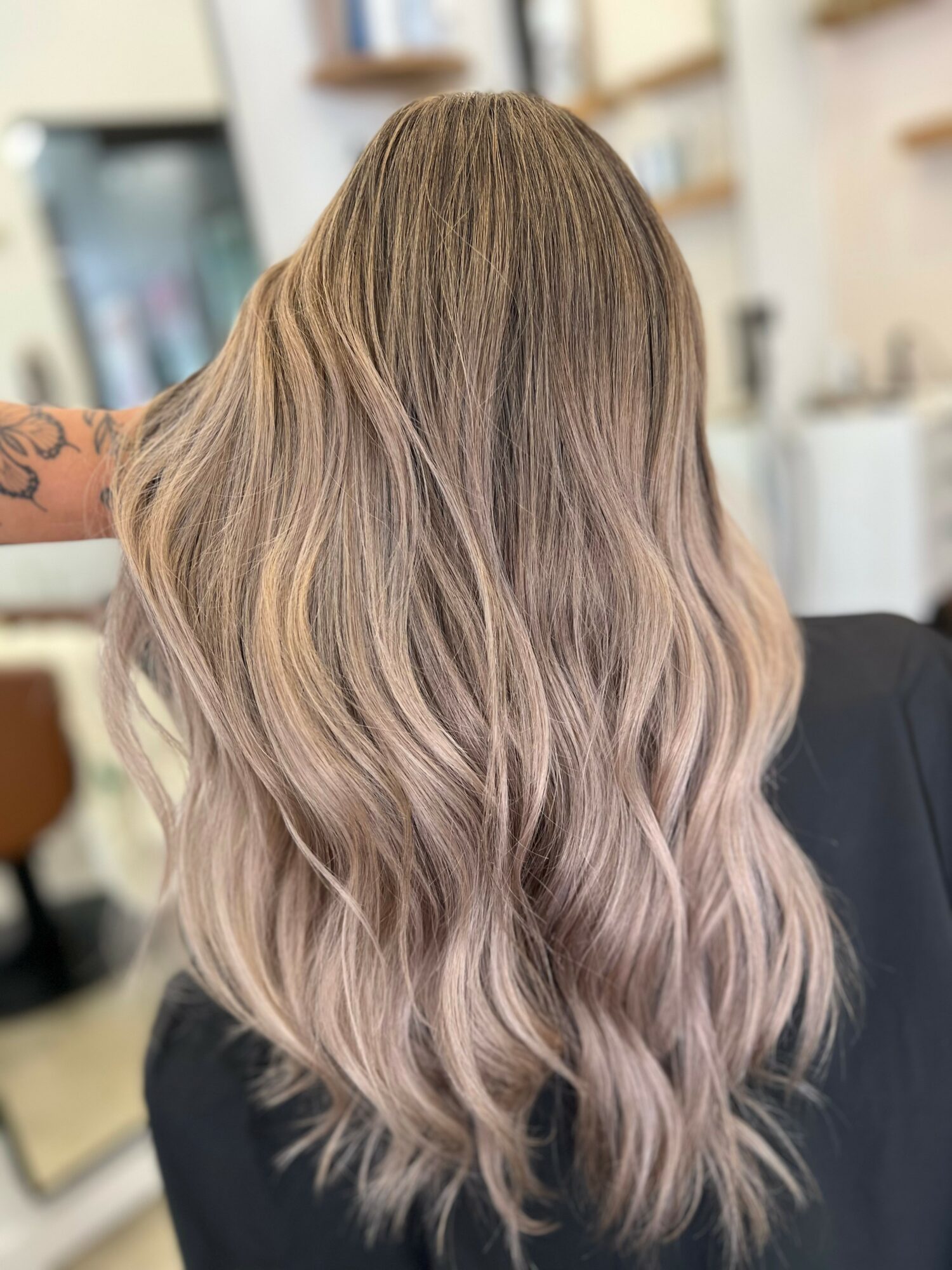 Person with long, wavy hair in shades of blonde and light brown, viewed from the back, indoors.
