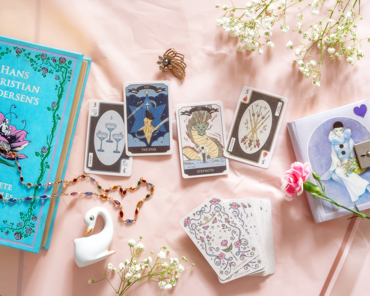 Cards, books, flowers, and decorative items arranged on a pink surface with a pink background.