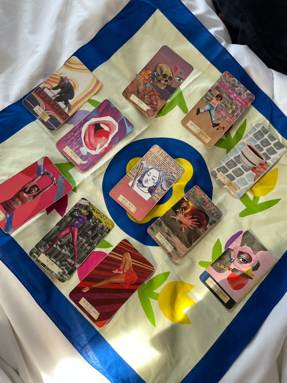 Colorful cards with various illustrations arranged on a cloth with a floral pattern, some overlapping, in a diagonal orientation.