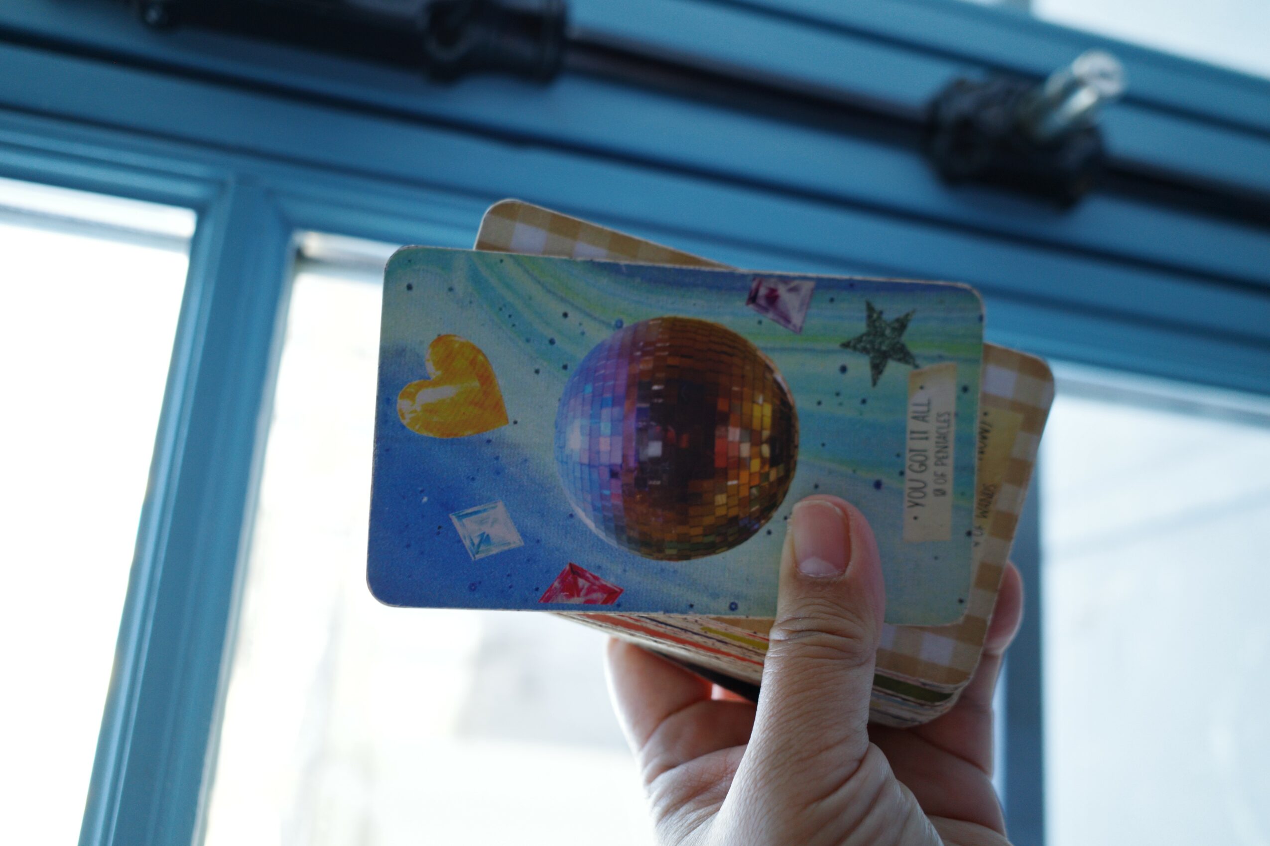 Hand holding a colorful card with a globe and starfish, in front of a window with blue blinds, daylight outside.