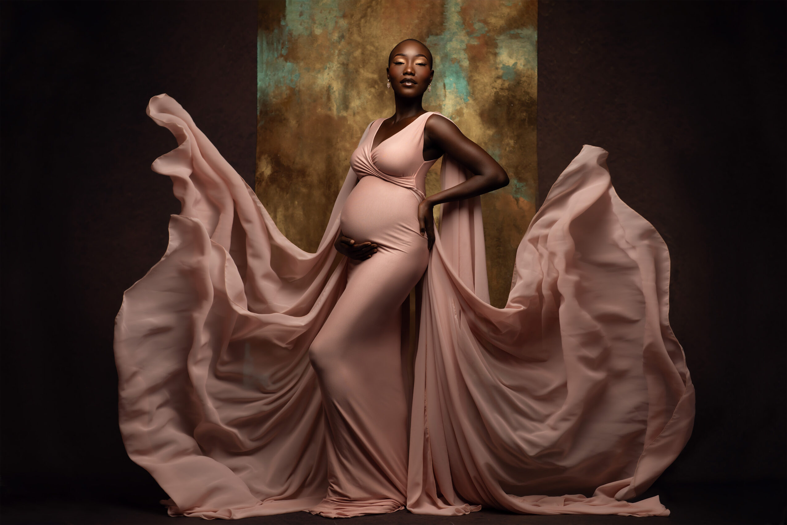 A pregnant woman in a flowing pink dress poses with fabric billowing around her, standing against a textured background.