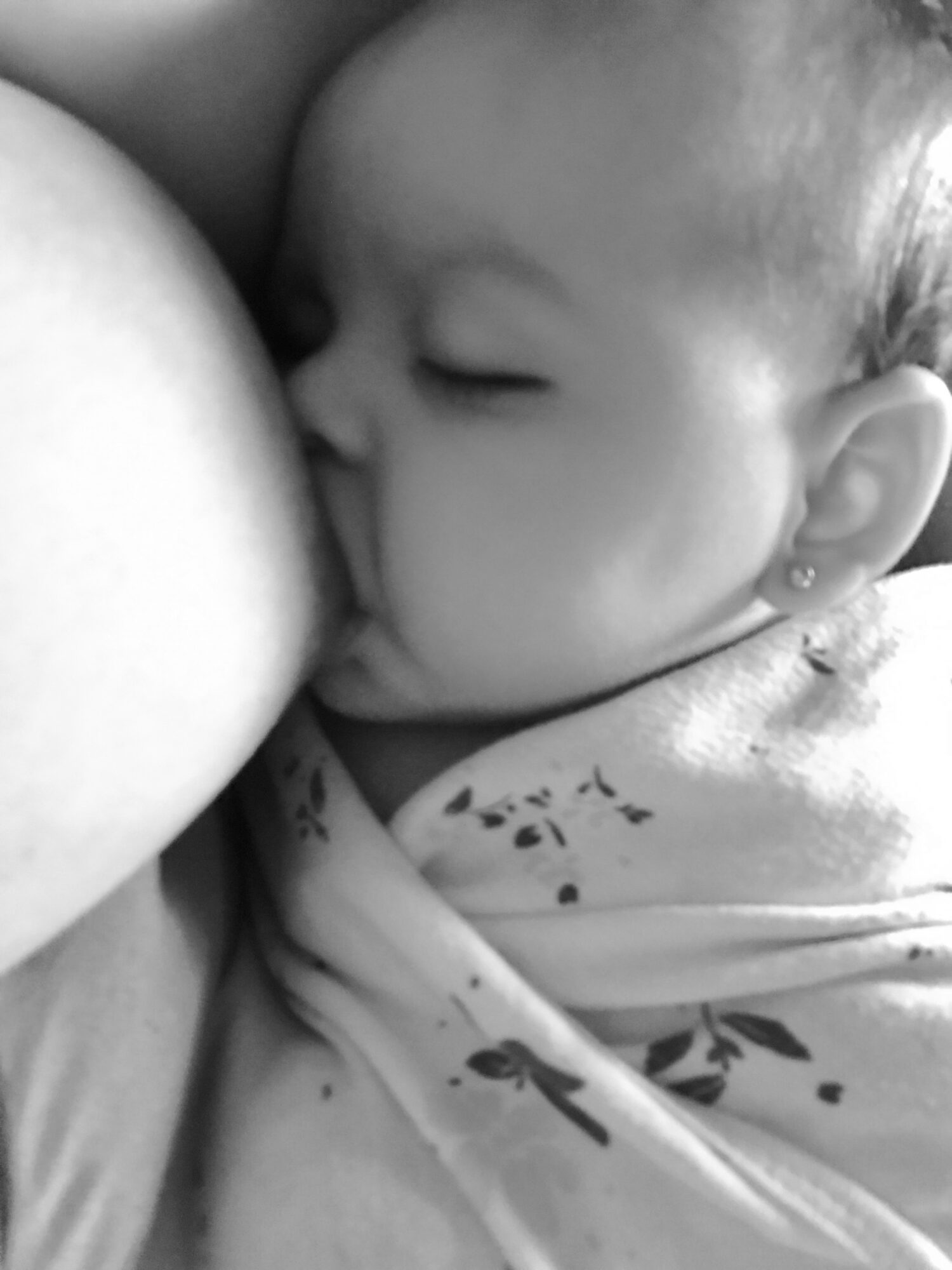 Baby breastfeeding, eyes closed, close-up of face and shoulder, in black and white.