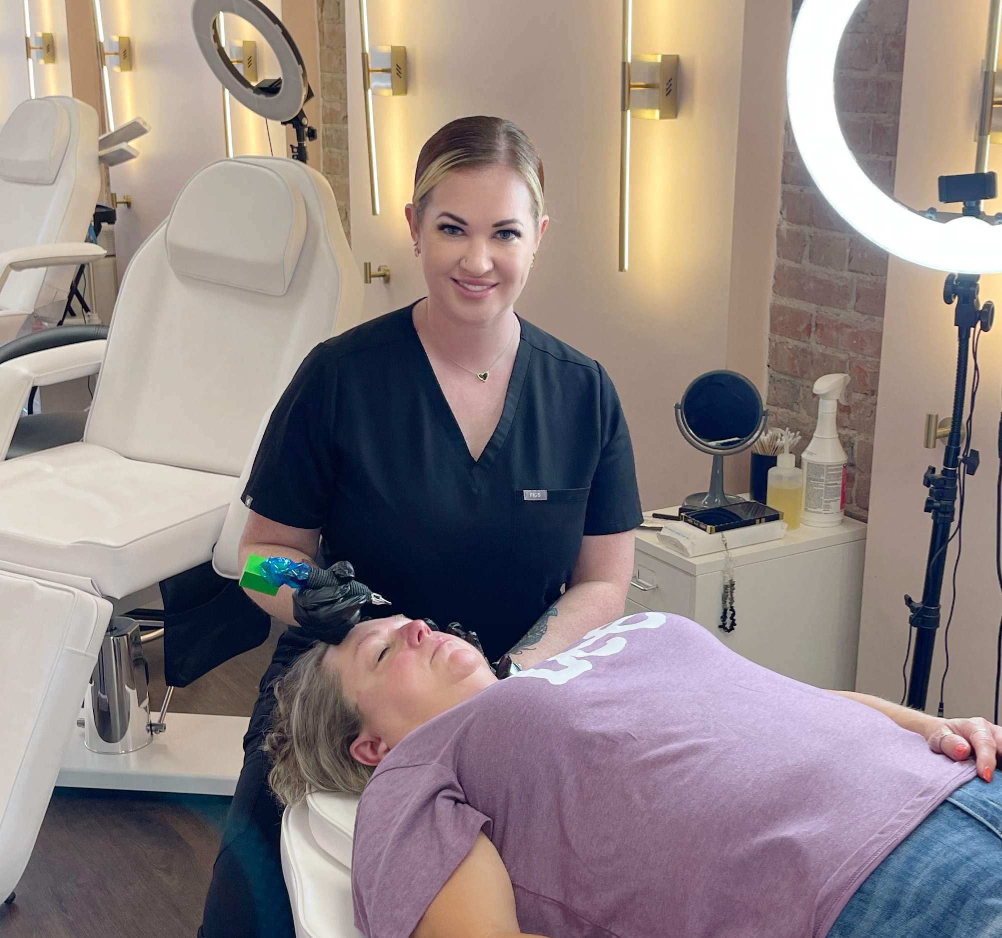 A woman in dark scrubs smiling at a patient lying on a treatment bed in a clinical setting.