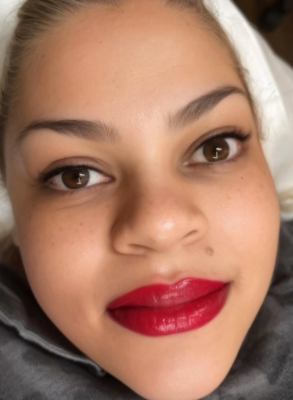 Close-up of a woman's face with makeup, smiling, with red lipstick and well-groomed eyebrows.