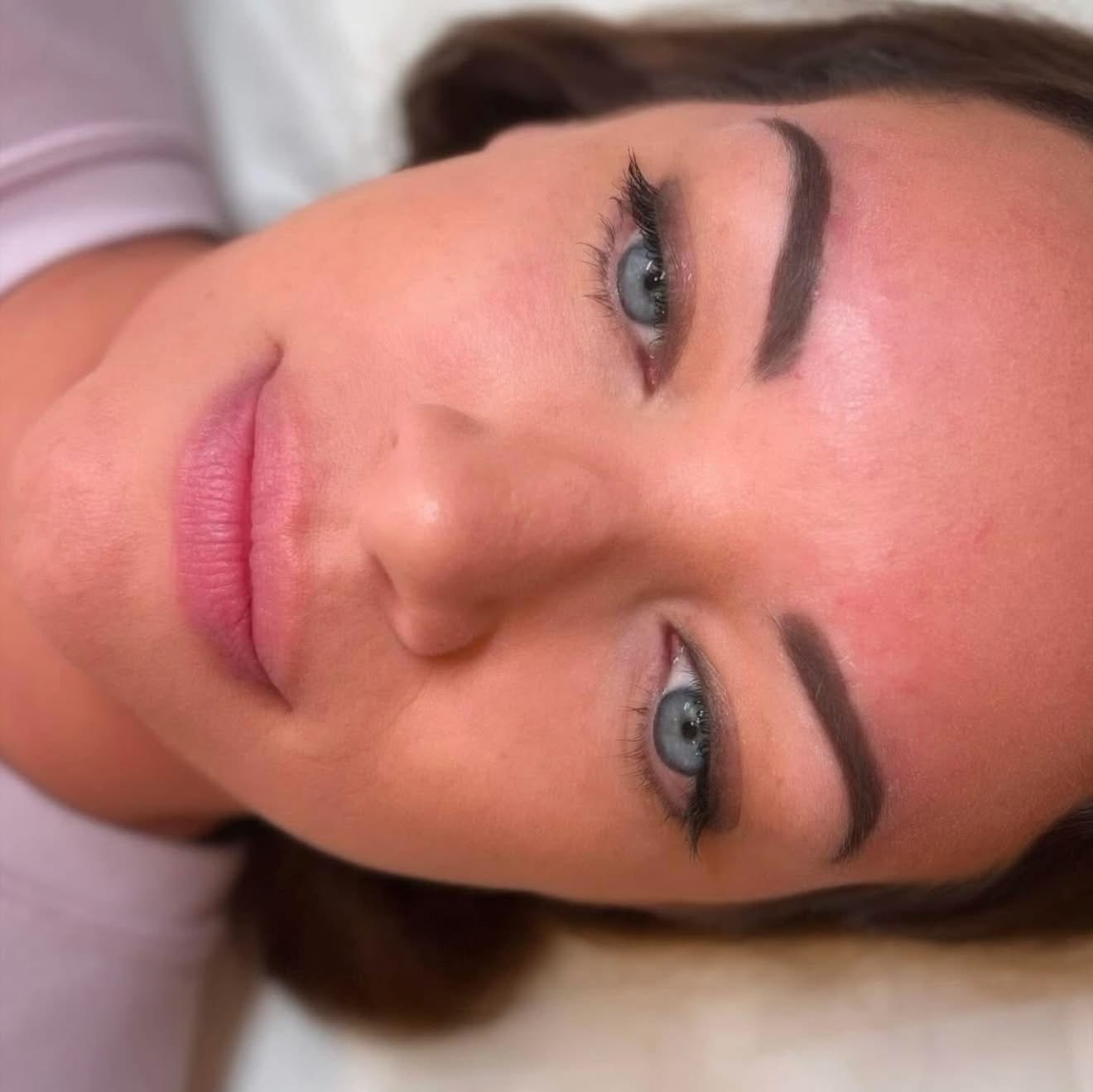 Close-up of a woman's face with makeup, lying down, with blue eyes and dark eyebrows.