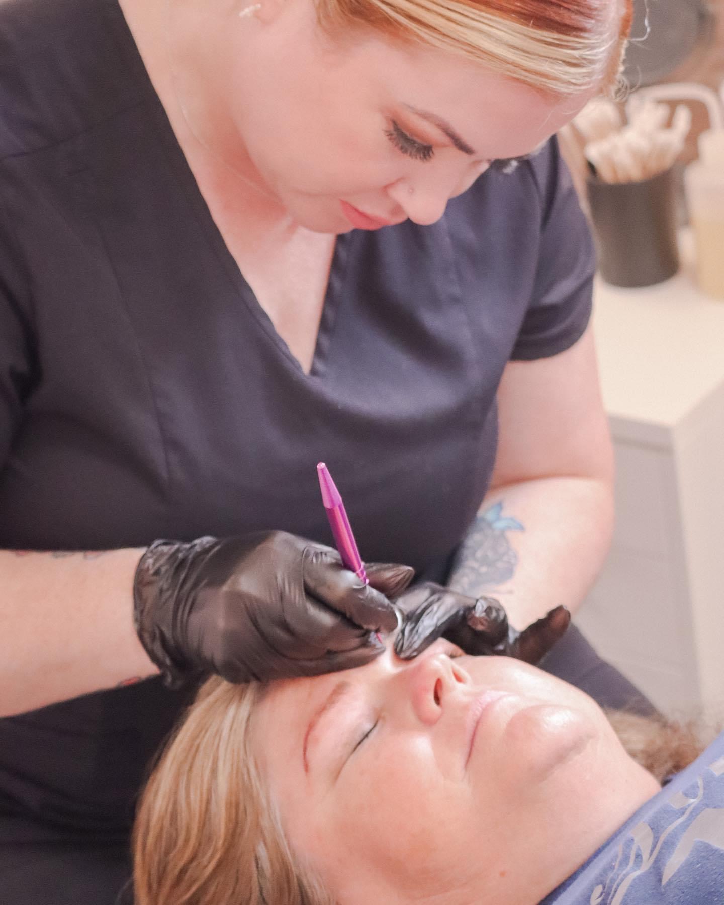 A woman with blonde hair receives a cosmetic treatment from a professional wearing black gloves.