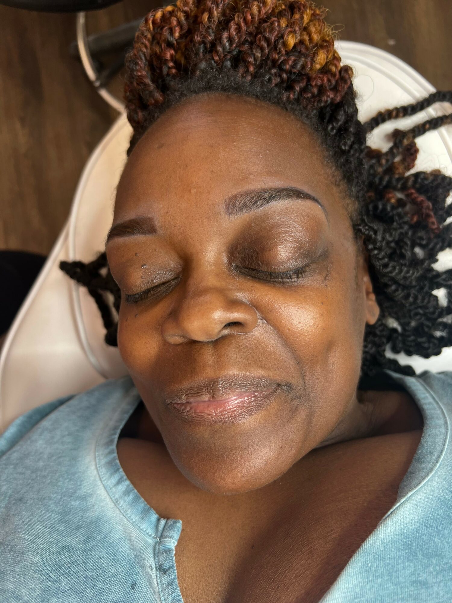 Woman with closed eyes and braided hair lying down, wearing a blue top.