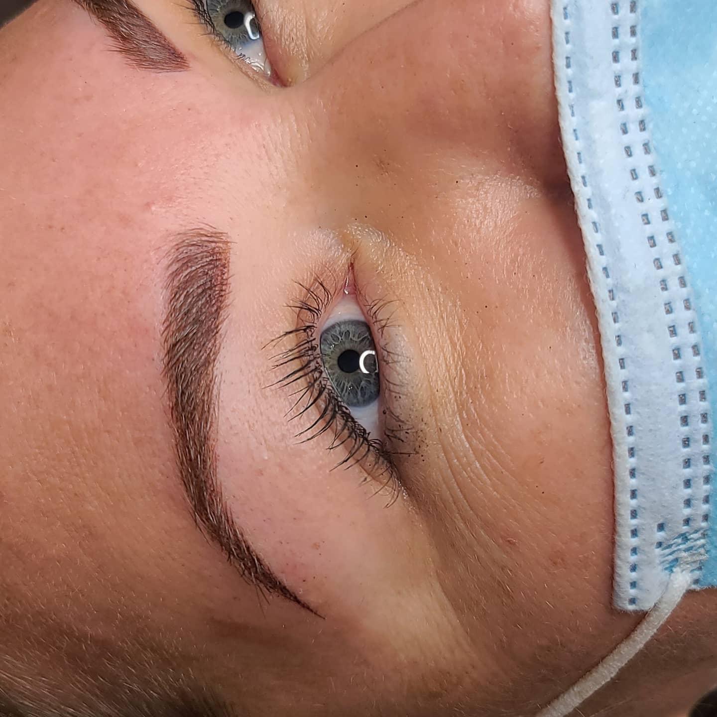 Close-up of a person's eye with makeup, partially covered by a blue face mask, showing eyebrow and eyelashes.