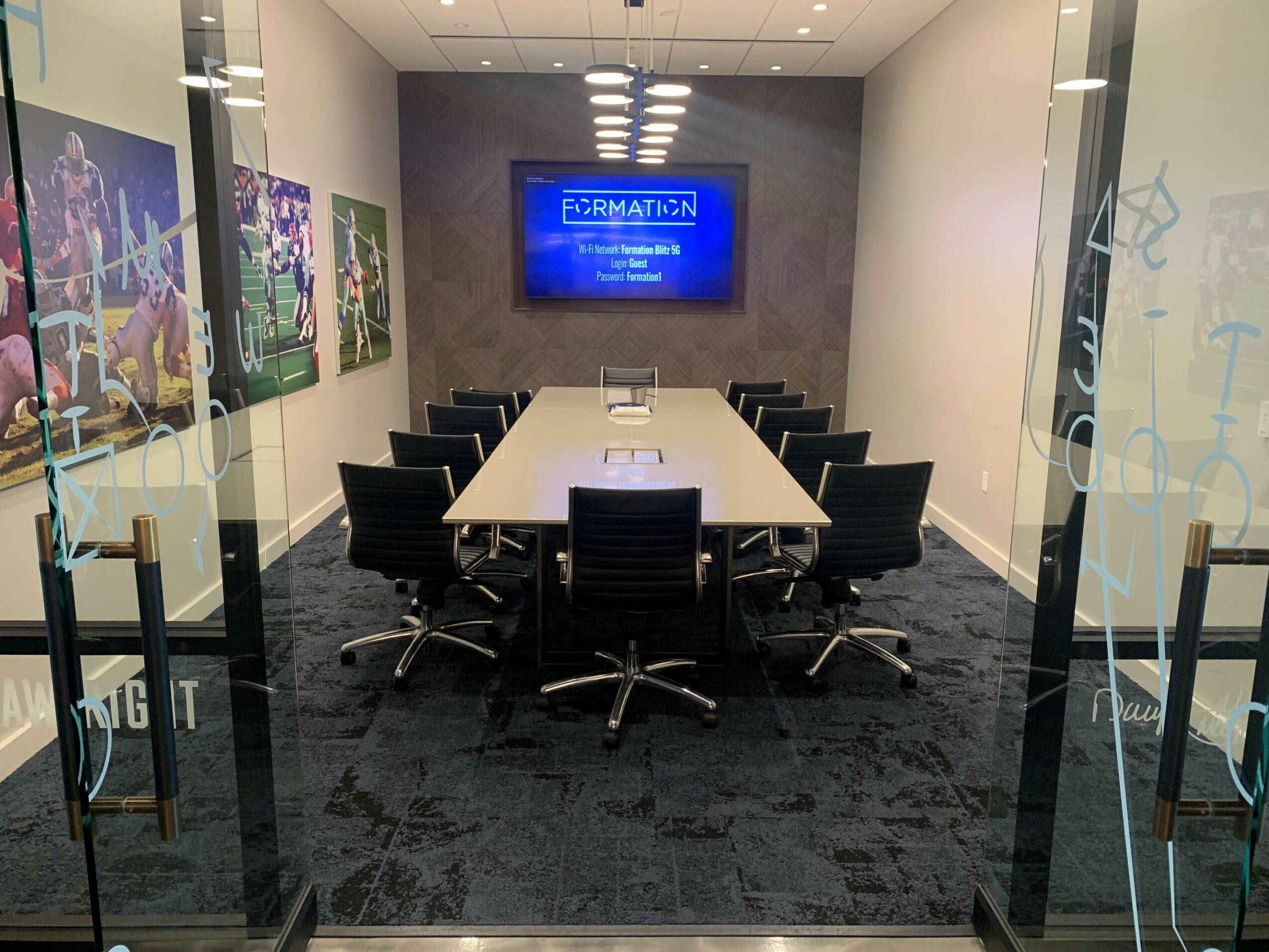 Conference room with a long table, chairs, a wall-mounted screen, and artwork on the walls.
