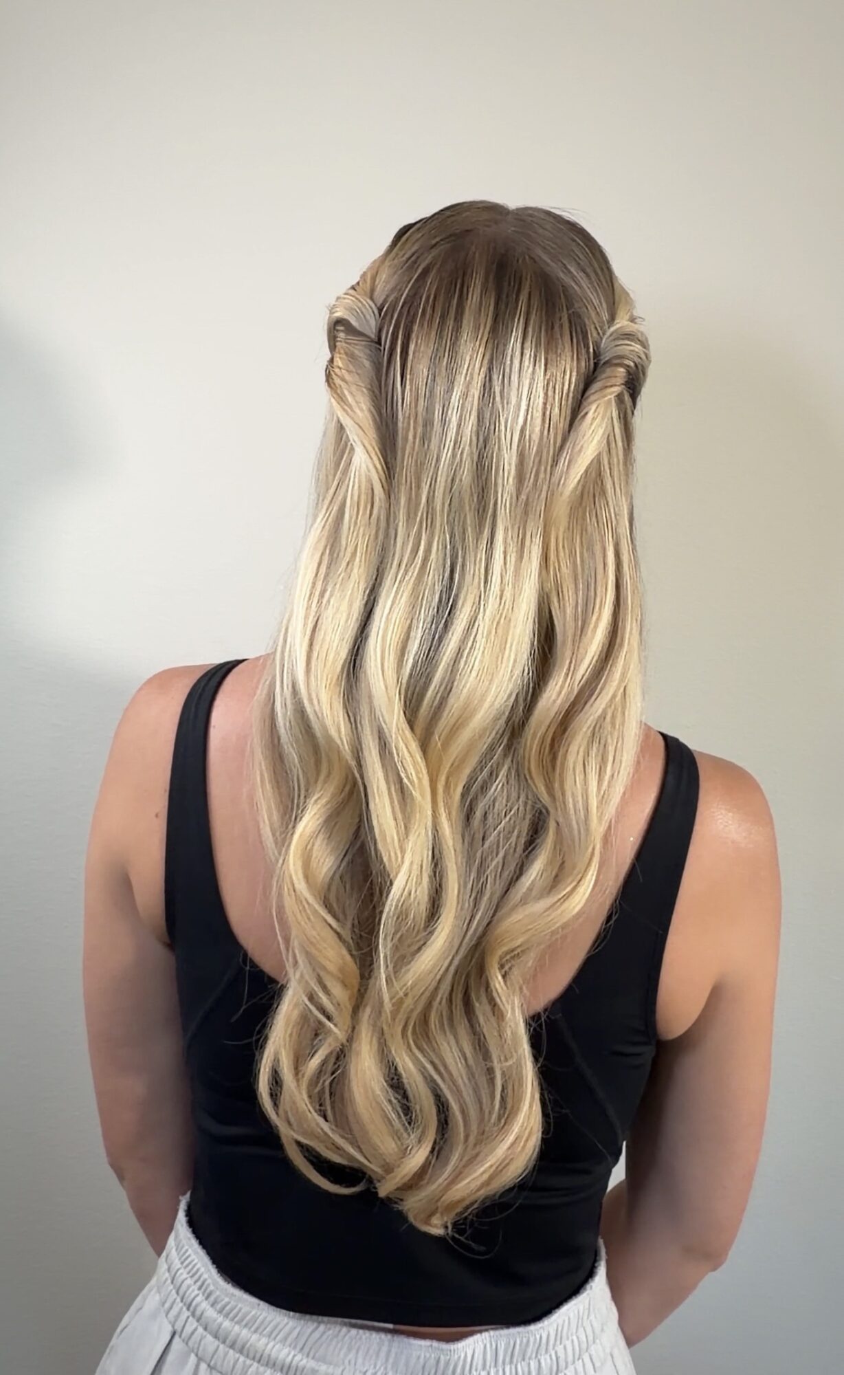 Back view of a woman with long, wavy blonde hair wearing a black sleeveless top.