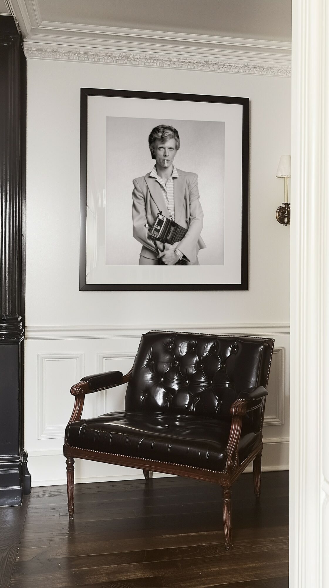 Black and white portrait of a woman hanging on a white wall above a dark leather armchair.
