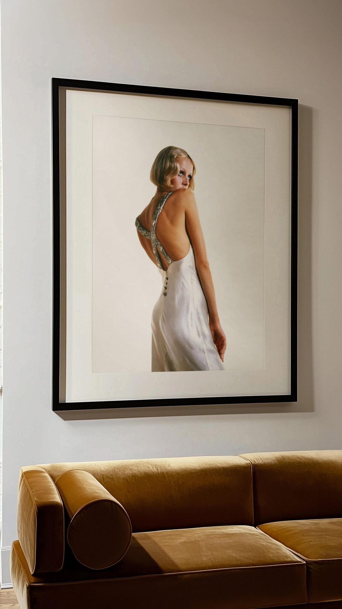 Framed photograph of a woman in a white dress, hanging on a wall above a yellow sofa.