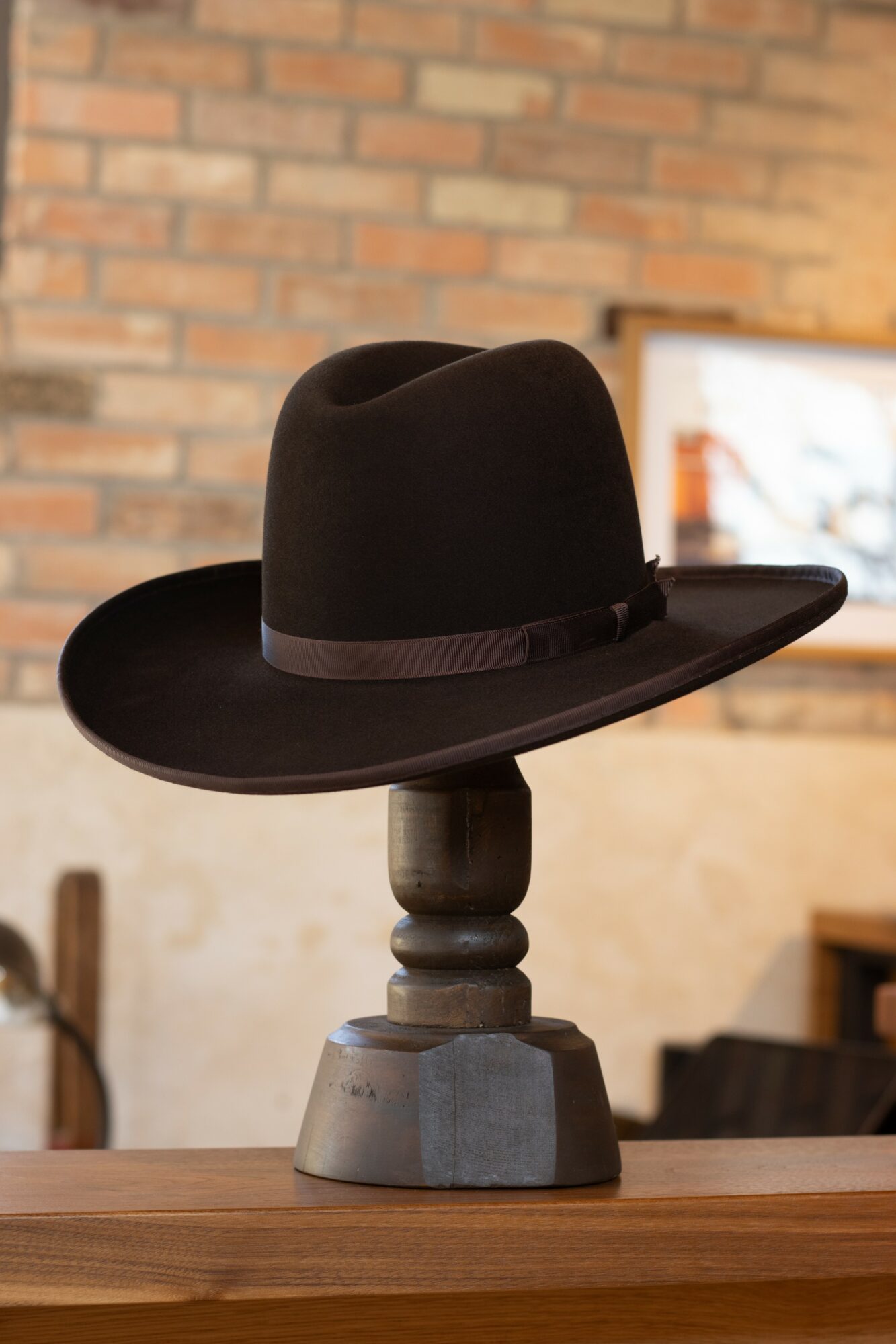 Black hat with a ribbon on a wooden stand against a brick wall background.