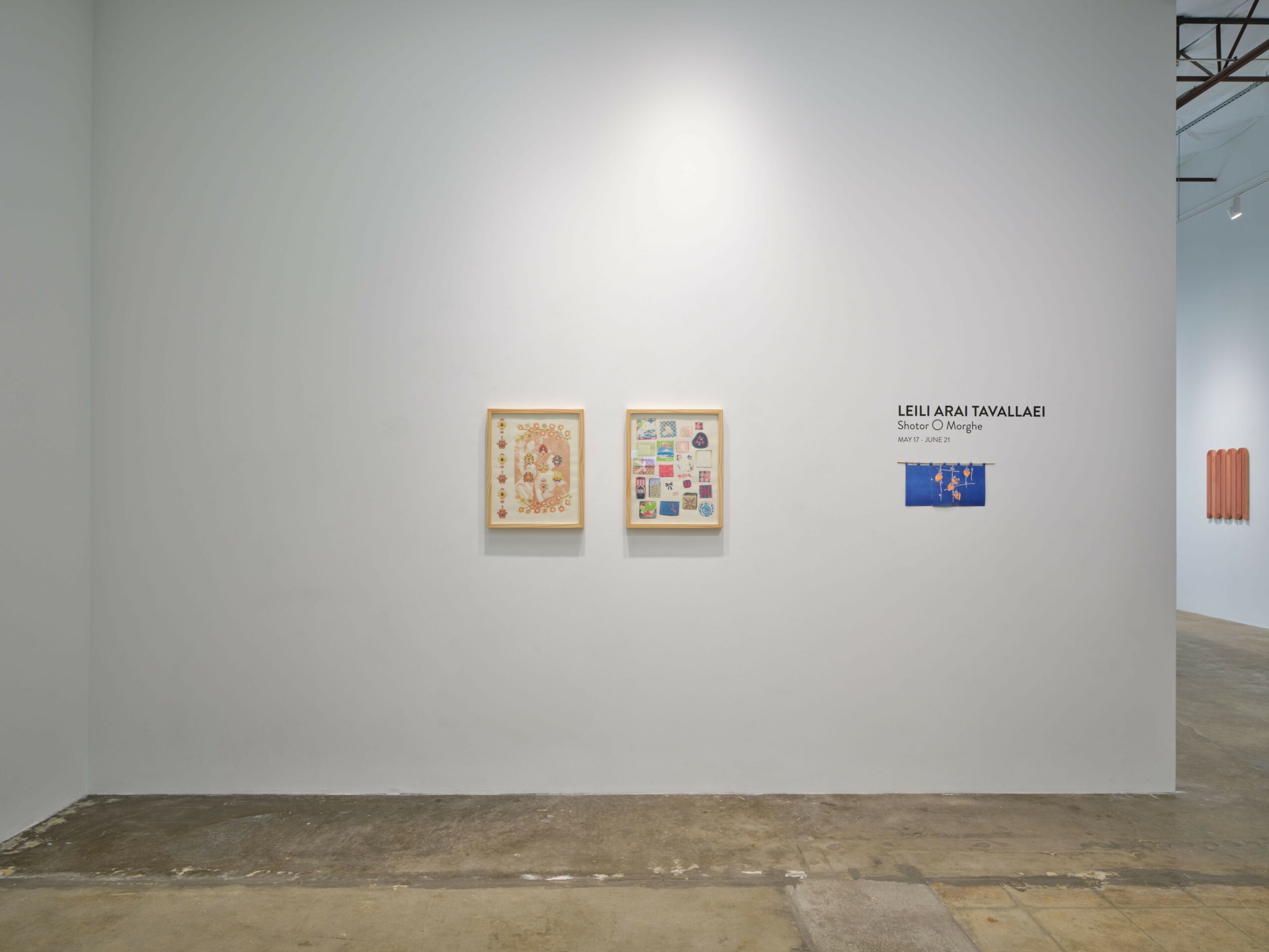 Two framed artworks hang on a white gallery wall, with a label and a small blue artwork to the right.