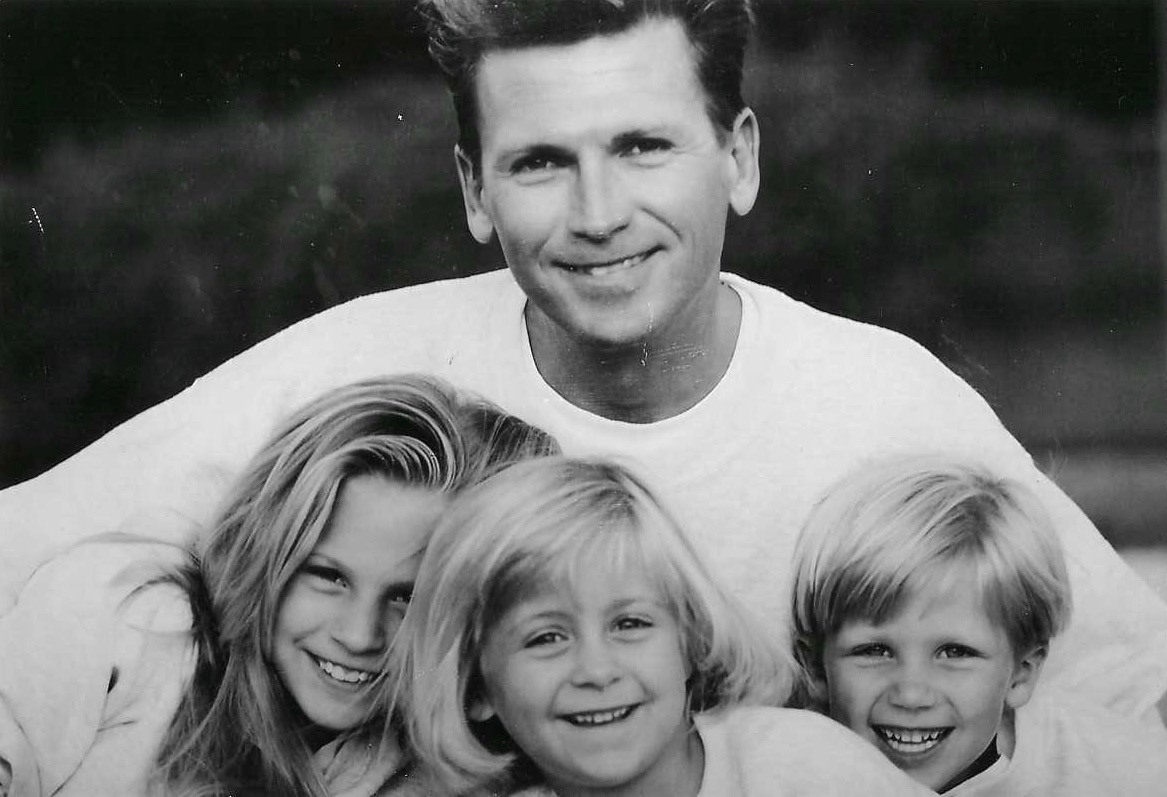 Black and white photo of a smiling man with three children, all smiling, outdoors background.