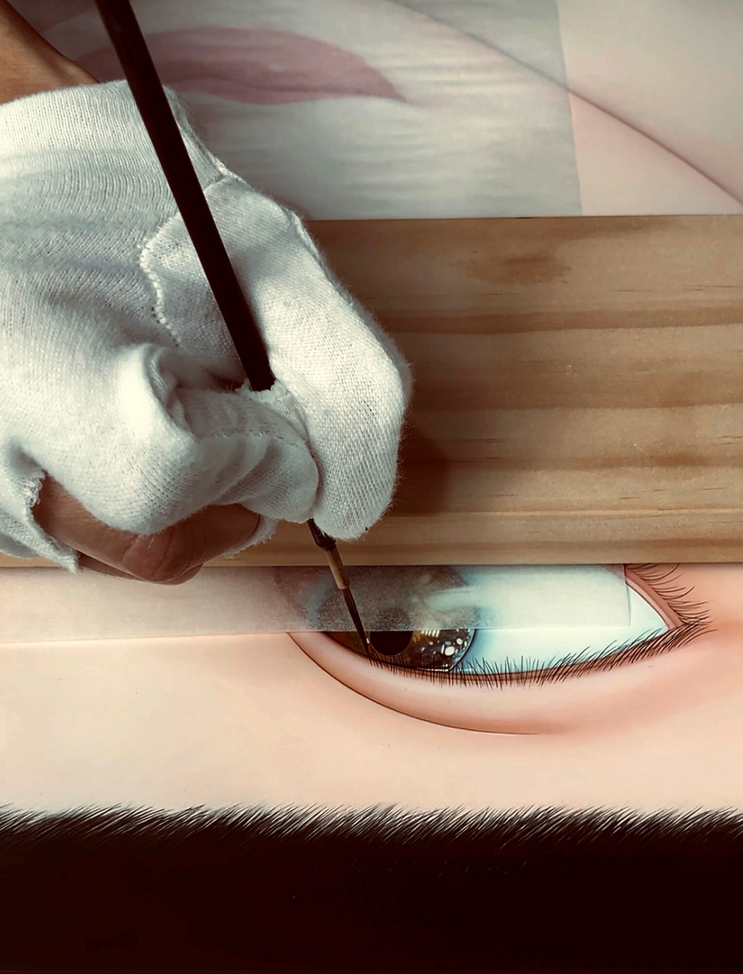 Person painting a realistic eye on a large canvas, holding a brush with a gloved hand, wooden surface nearby.