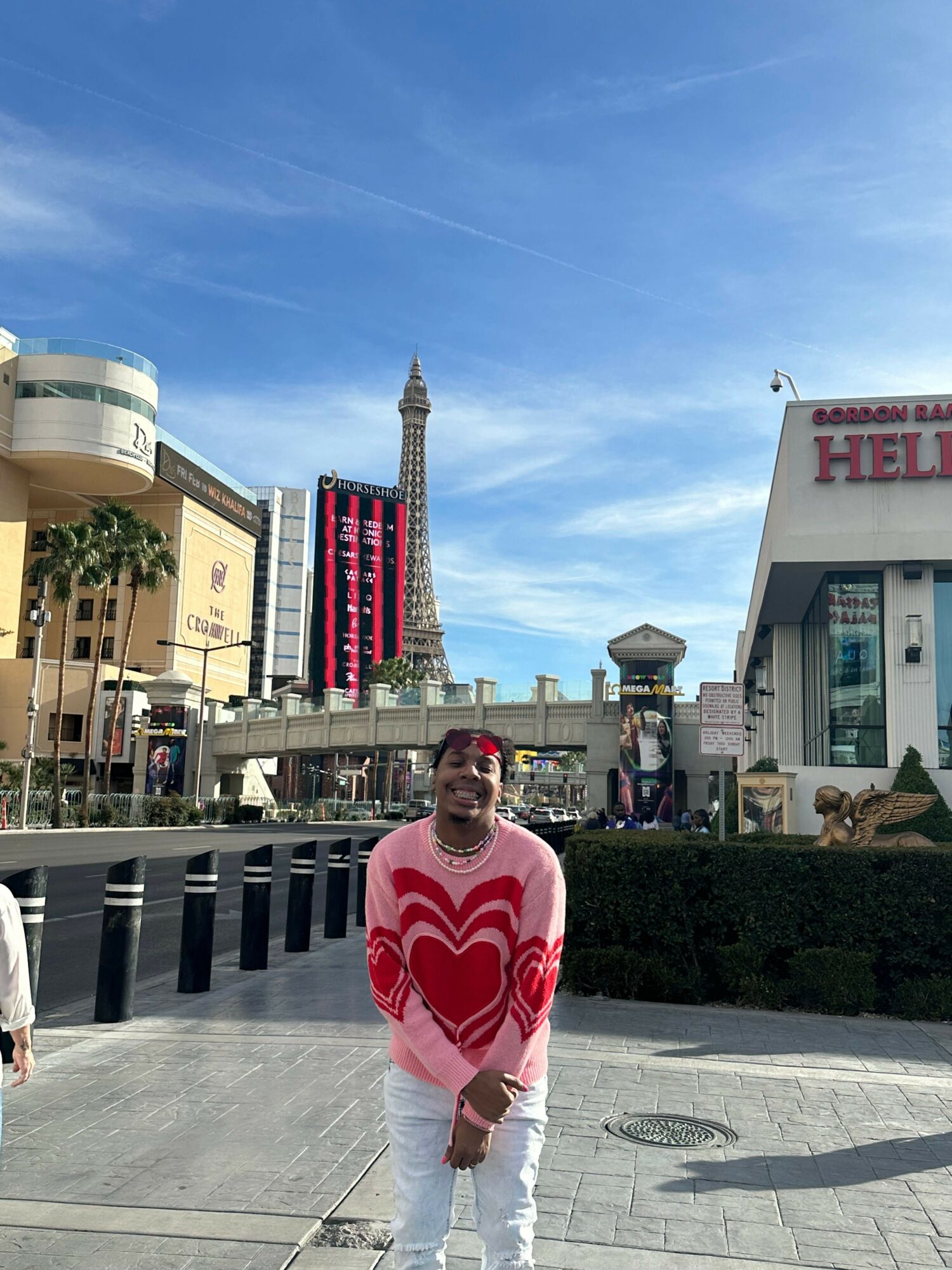Person standing on sidewalk in front of a cityscape with a tall tower, buildings, and a clear blue sky.
