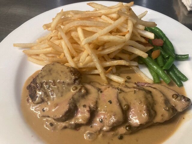 Plate with French fries, green beans, and sliced meat with creamy sauce.