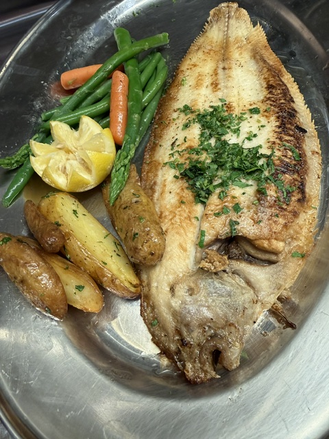 Grilled fish with green beans, carrots, lemon, potatoes, and mushrooms on a metal plate.