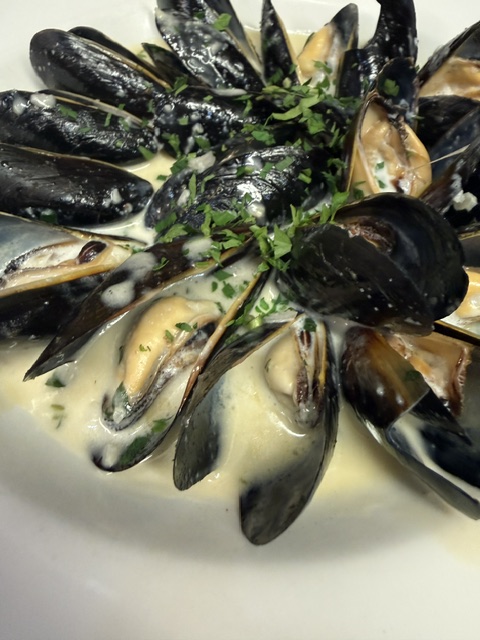 A dish of cooked mussels with green herbs and creamy sauce, served on a white surface.