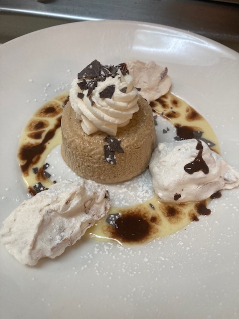 Dessert with ice cream, whipped cream, chocolate shavings, and sauce on a white plate.