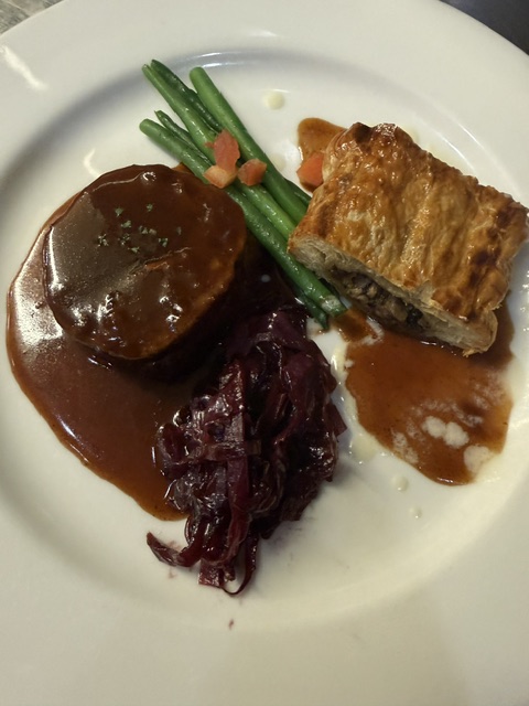 Fried meat with green beans, a dark sauce, and a side of cooked purple vegetables on a white plate.