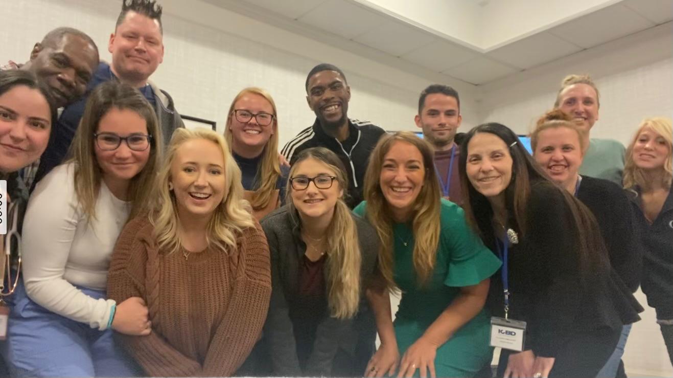 Group of diverse people smiling and posing together indoors, some wearing glasses and name tags.