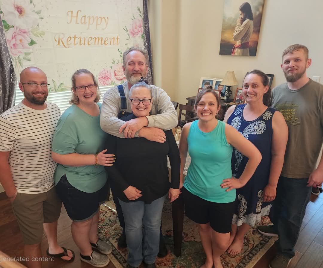 Group of seven people celebrating retirement indoors, smiling, with a 'Happy Retirement' sign in the background.