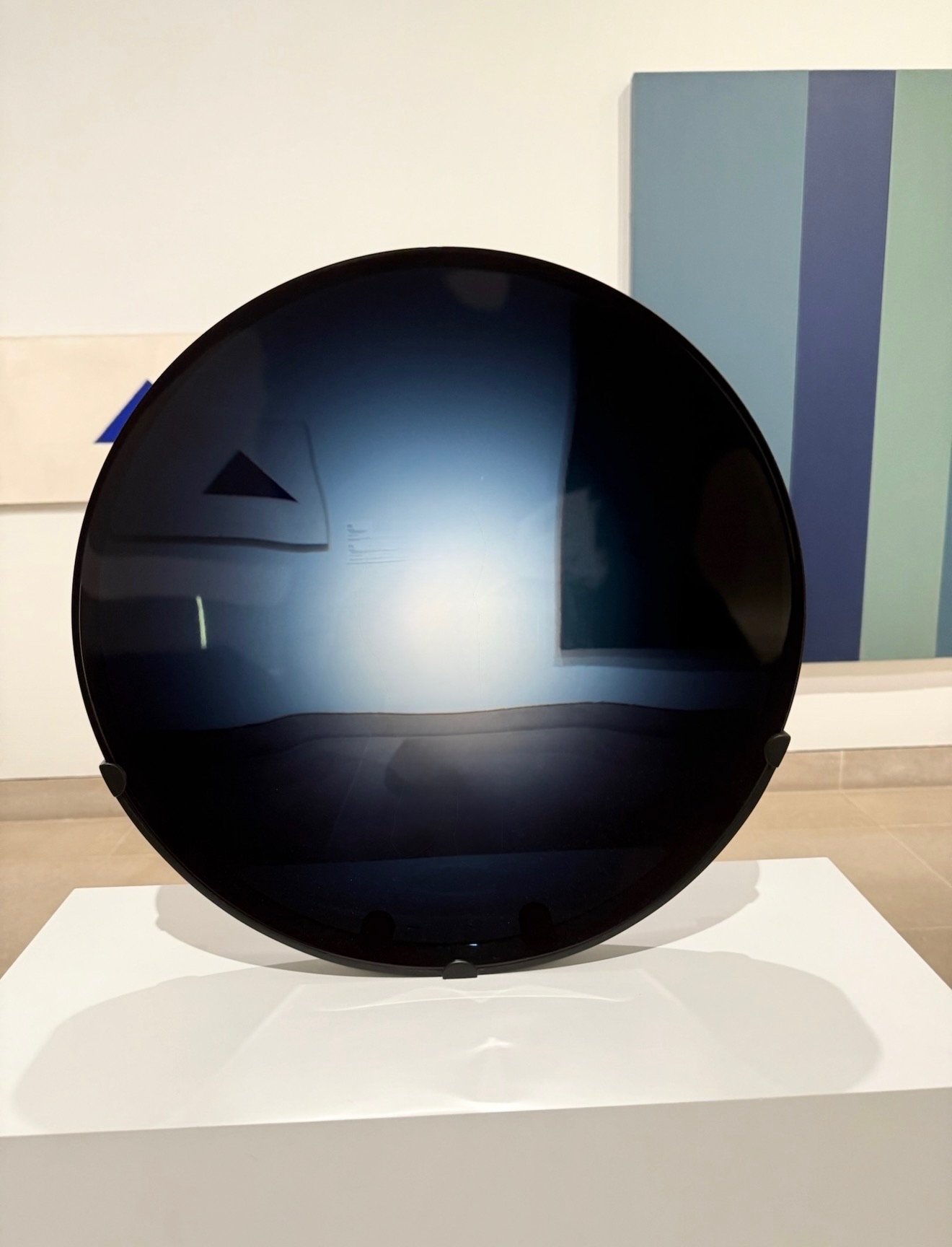 Glossy black spherical object on a white surface, with a reflection of a window and a blue wall in the background.