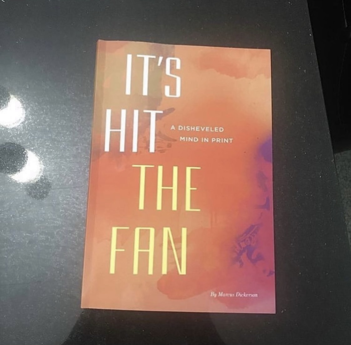 Book cover with orange and purple background, title 'IT'S HIT THE FAN', subtitle 'A DISHEVELED MIND IN PRINT', author 'Mona Delorme'.
