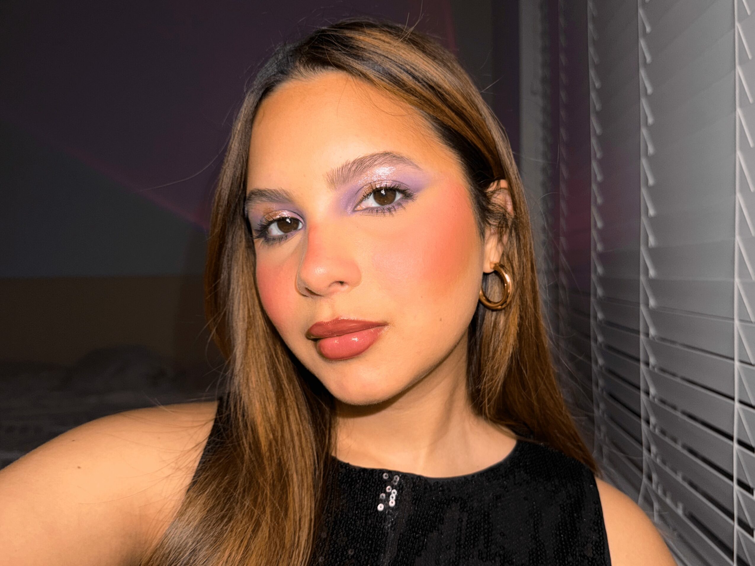 Portrait of a woman with long hair, makeup, and earrings, wearing a black top, looking at the camera.