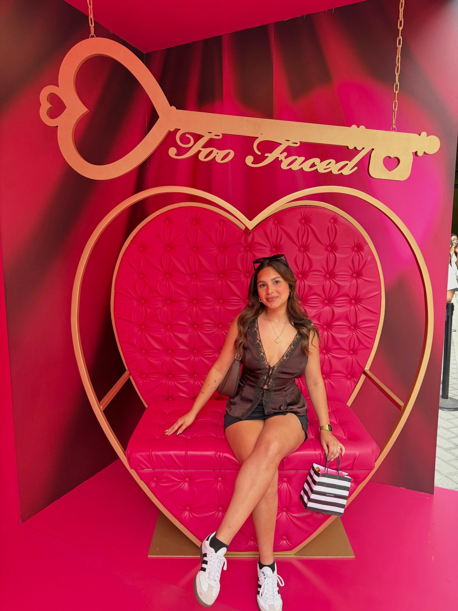 Woman sitting on pink heart-shaped seat inside a large key-shaped frame, with red curtains in background.