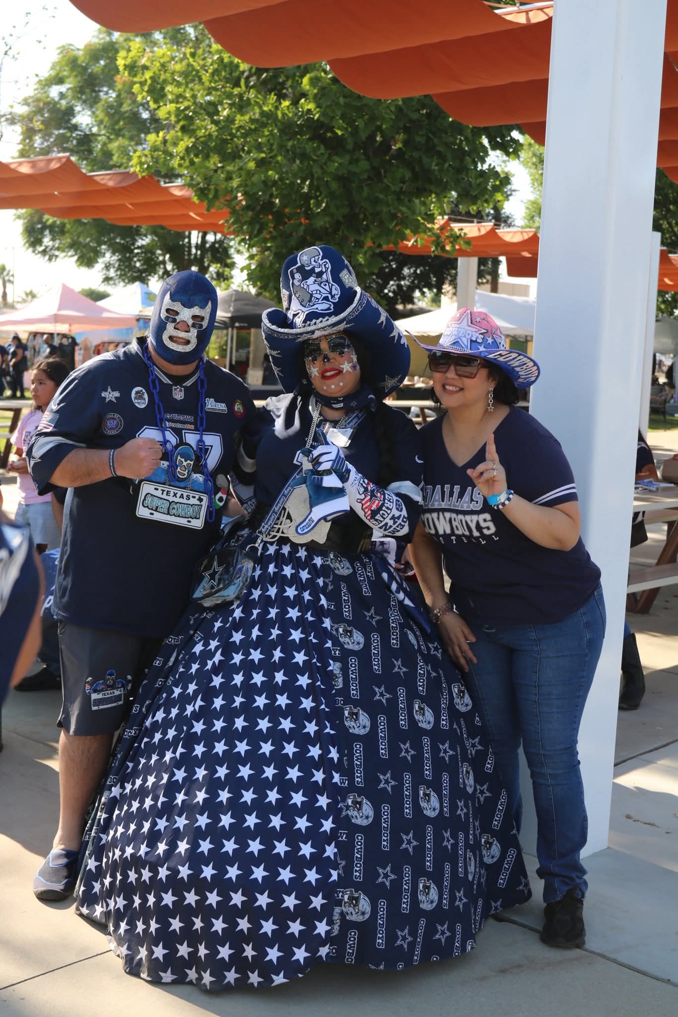 Three people with a woman in a star-patterned dress and two others in blue shirts, outdoors under orange umbrellas.