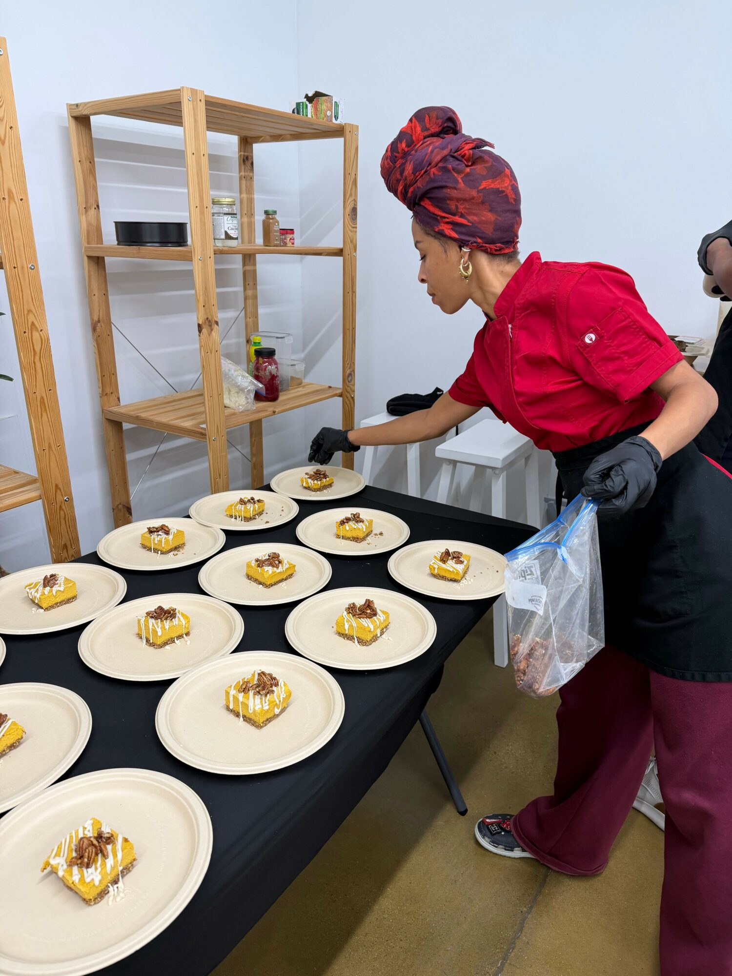 Two people preparing desserts on a table with plates, one wearing a red hoodie and the other a patterned headscarf.